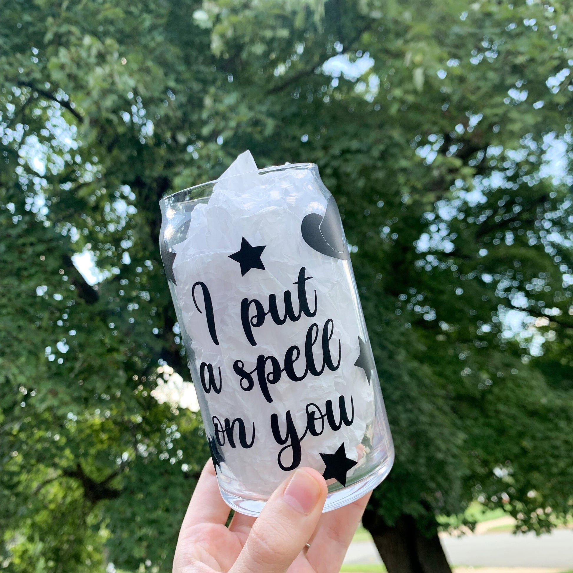 Hand holding I put a spell on you glass cup with stars and a witch's hat.