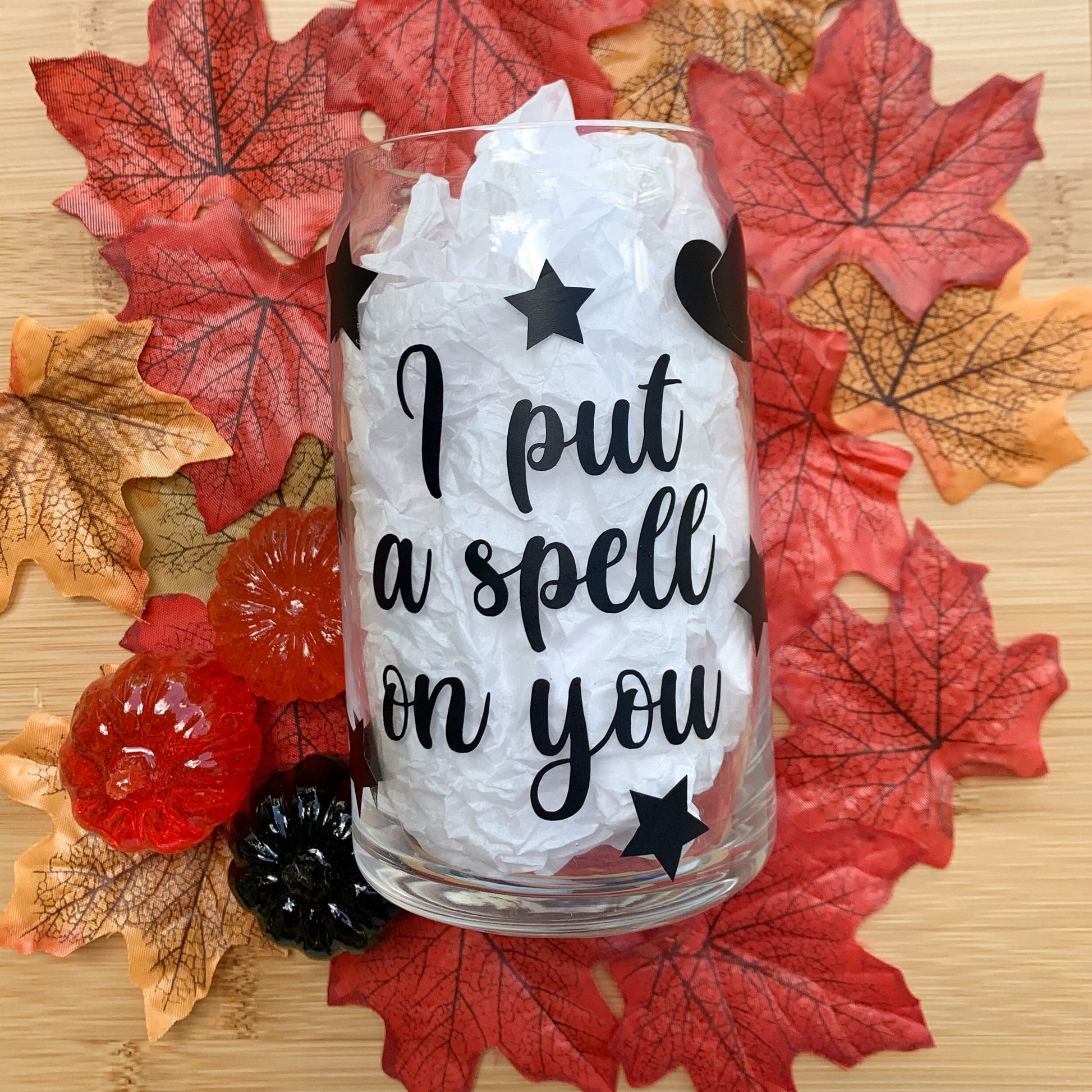 Halloween glass cup with stars and witch's hat laying on colorful leaves.