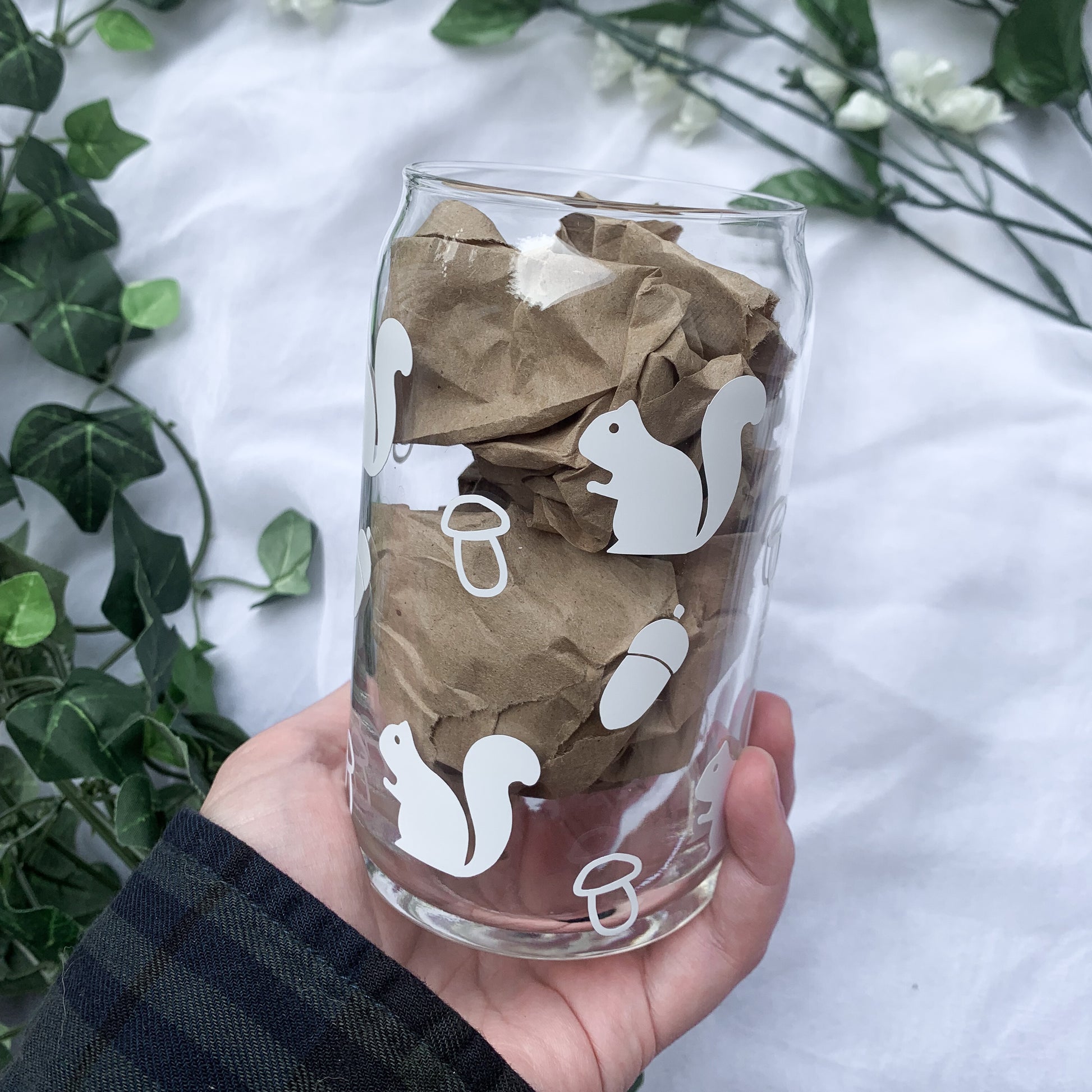 A glass beer can stuffed with crinkle paper being held by a hand. 