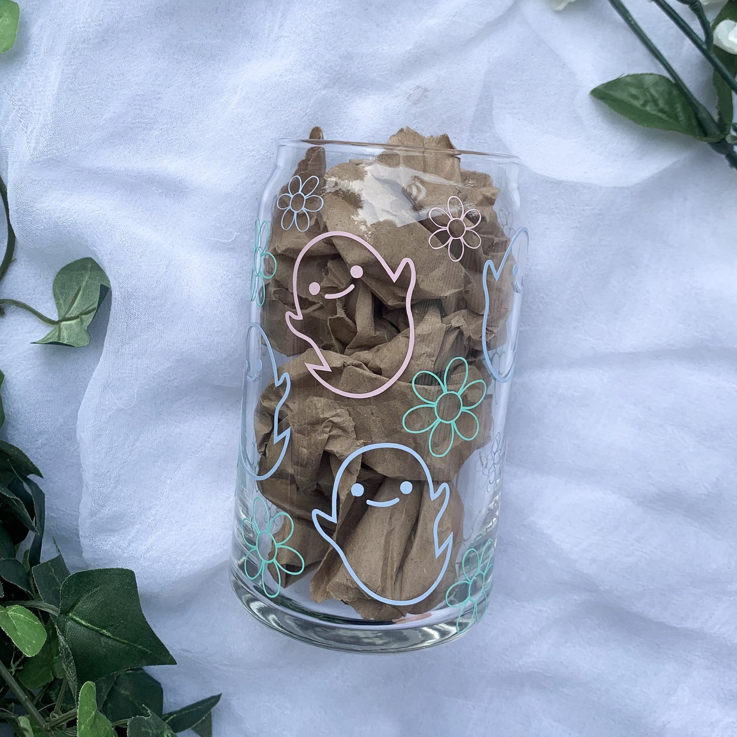 An glass can with pastel pink and blue ghosts is laying on a white background.