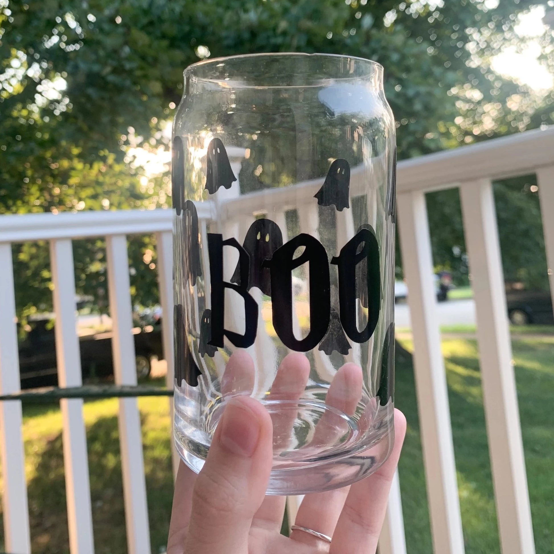 Cute boo ghost glass soda can being held by a hand in front of greenery.