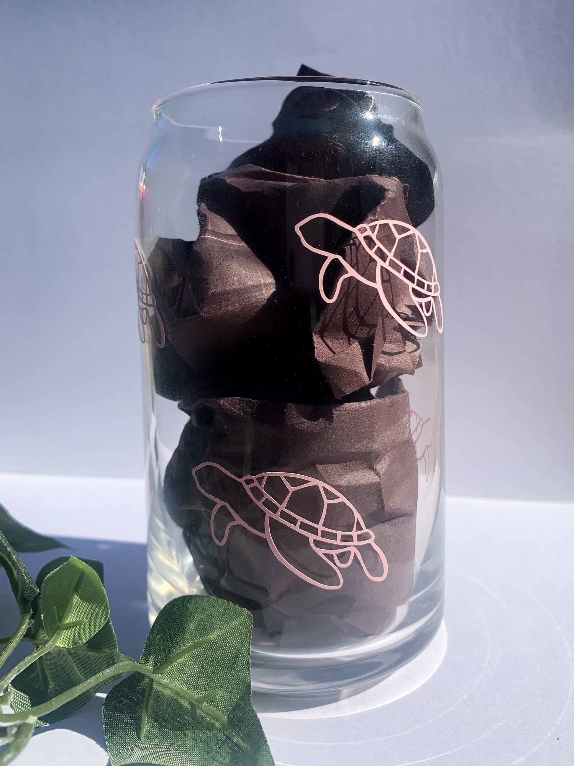 Aesthetic product photo of pink sea turtle glass in front of white backdrop and stuffed with black paper.