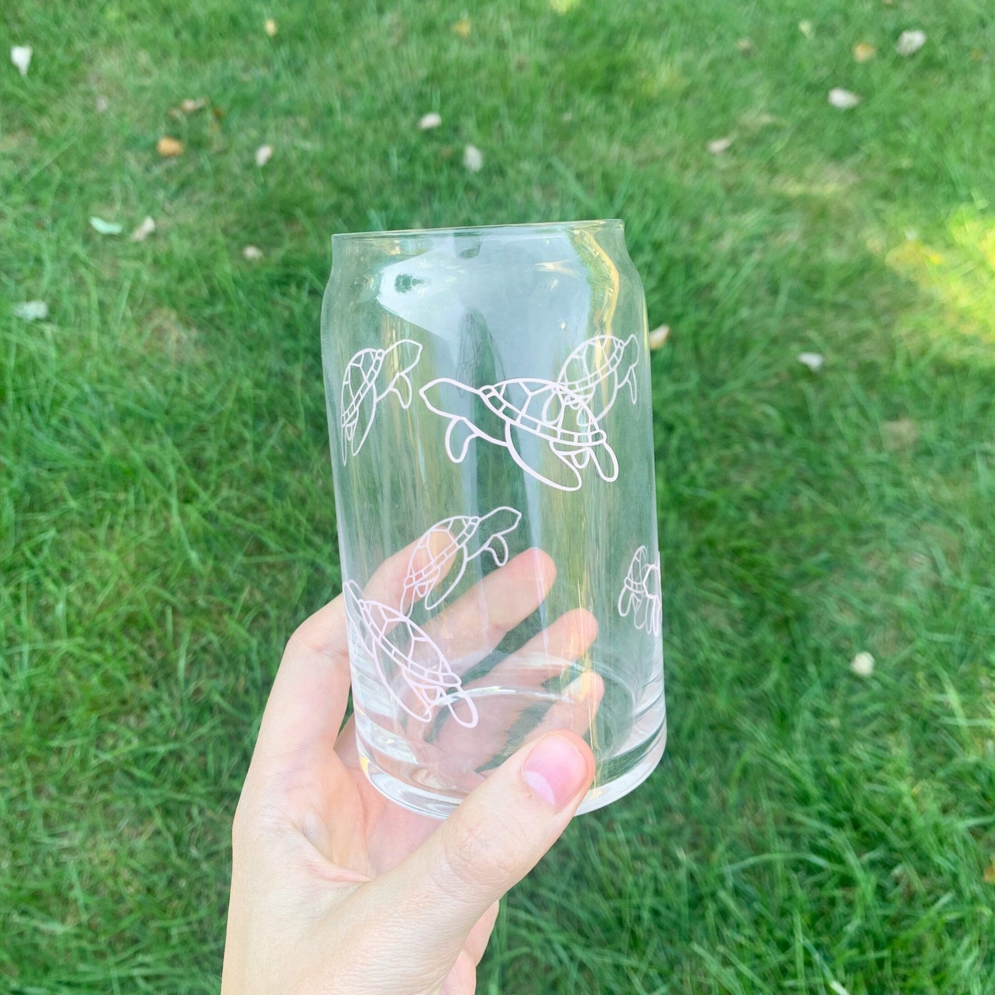Ocean life glass with pink sea turtle outlines all around it being held in a hand over grass.