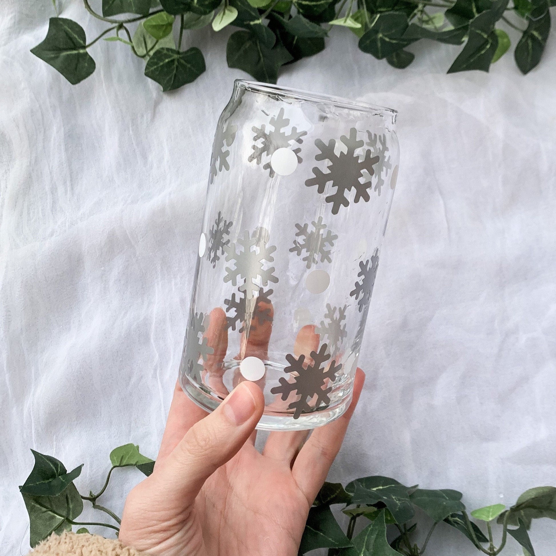 An adorable winter glass cup being held above a simple white background with ivy vines.