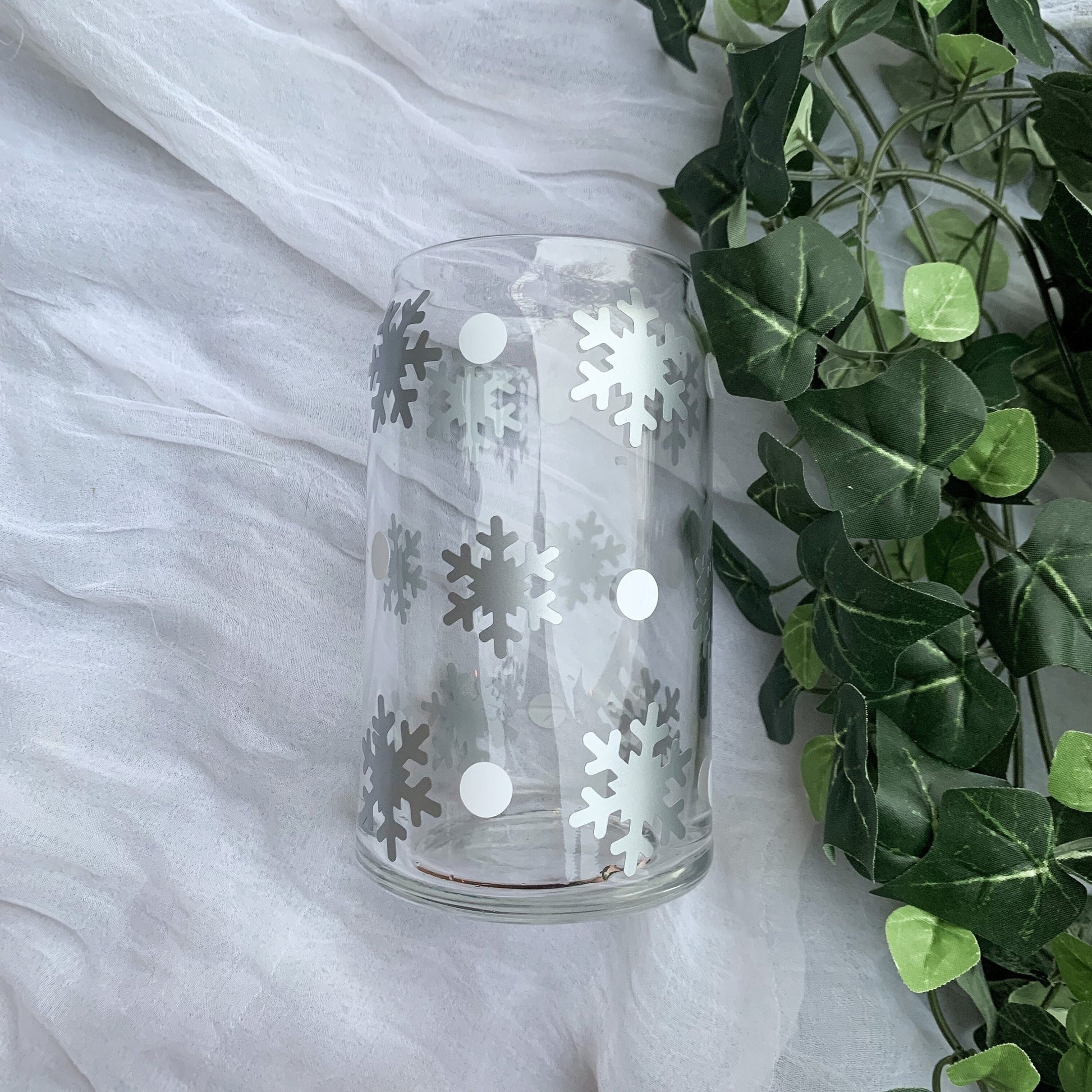 Clear glass can laying on a white background next to green ivy leaves.